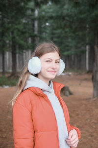 Beautiful teenager girl wearing red jacket and earmuffs  in the park. schoolgirl in the forest.