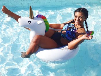 High angle portrait of smiling young woman sitting on inflatable ring in swimming pool