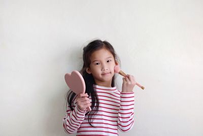 Portrait of cute girl holding pink while standing against white background