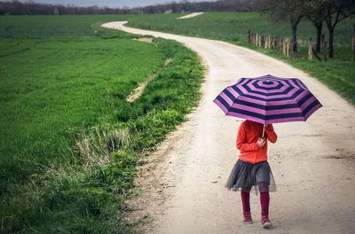 Rear view of woman with umbrella walking on road