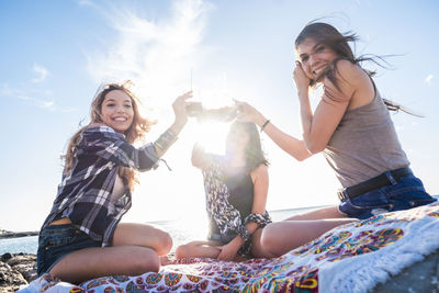 Portrait of happy female friends toasting drinks at beach