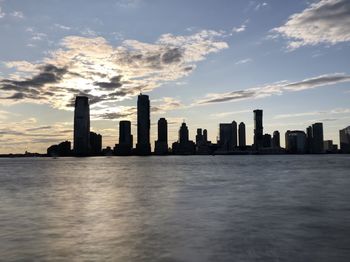 Sea by modern buildings against sky during sunset