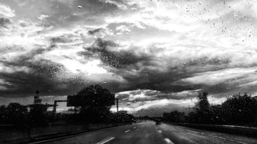 Road against sky seen through wet car windshield