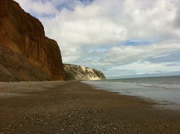Cliffs at beach against cloudy sky