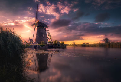 Scenic view of traditional windmill reflecting on calm river against cloudy sky