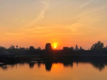 Silhouette buildings by lake against romantic sky at sunset