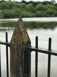 Close-up of metal railing by river against sky