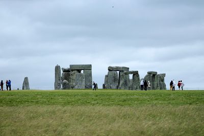 People standing by stonehenge against cloudy sky