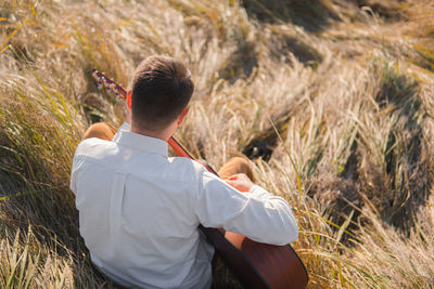 Man with acoustic guitar sits in the autumn grass, tranquil scene