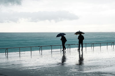 Silhouette people walking on beach against sky