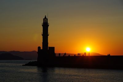 Silhouette lighthouse by sea against sky during sunset