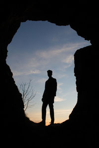 Silhouette man standing on rock against sky during sunset