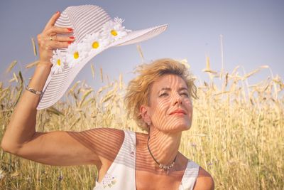 Woman holding hat by plant against sky