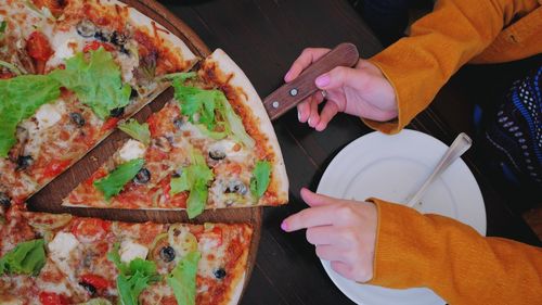 Cropped hand of woman holding pizza on table