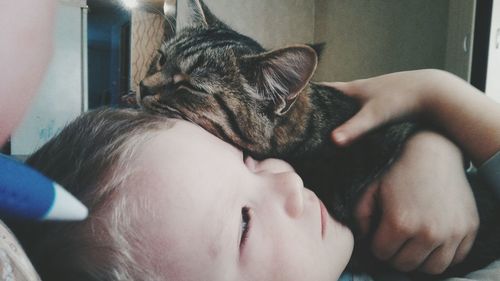 Close-up of boy with cat lying at home