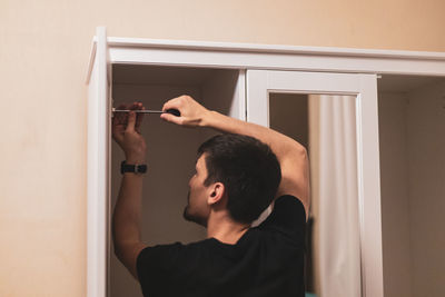 A young man is tightening the screws on the fittings inside the wardrobe.