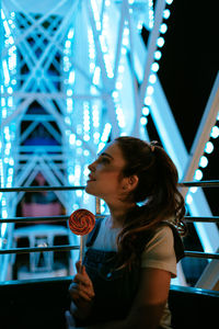 Portrait of young woman looking at illuminated camera at night