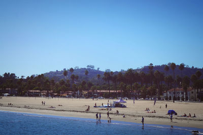 People on beach against clear blue sky