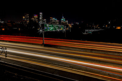 High angle view of light trials against illuminated cityscape at night