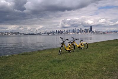 Bicycle by river in city against sky