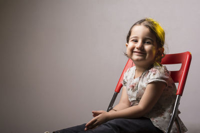 Portrait of a smiling girl sitting against wall