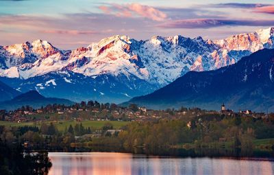Lake with trees and houses against snowcapped mountains 