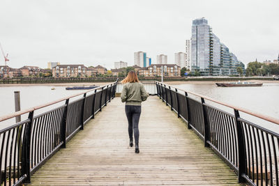 Rear view full length of woman walking over river on footbridge in city