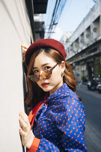 Portrait of young woman wearing sunglasses against wall outdoors