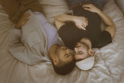 High angle view of gay couple lying on bed with eyes closed resting at home