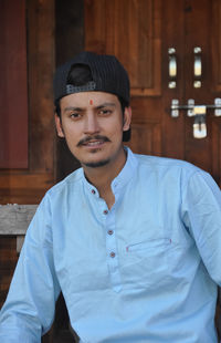 Closeup of a handsome indian young guy wearing cap backwards, looking at camera while sitting 