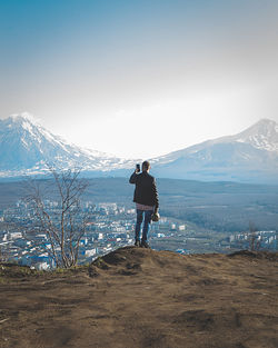 Rear view of man standing on snowcapped mountain against sky