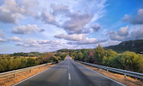 Empty road along trees and plants against sky