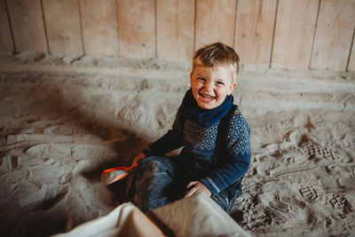 Little boy smiling playing in sand in winter with shovel in hand