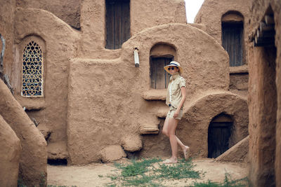 Portrait of a traveler woman in a hat and sunglasses stands in an abandoned eastern city made 