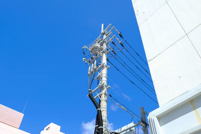 Low angle view of telephone lines amidst buildings against blue sky