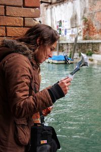 Side view of woman reading paper by canal