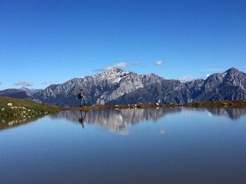 Scenic view of sea by mountain against blue sky