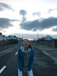 Full length of young woman standing on road against sky