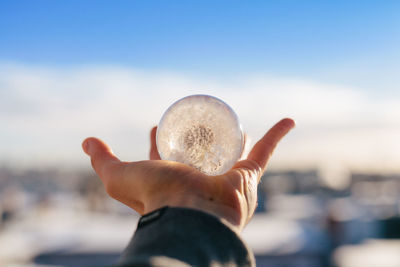 Close-up of hand holding crystal ball against sky