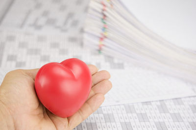 Cropped hand of cardiologist holding heart model by papers