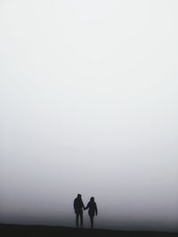 Silhouette couple standing against sky during foggy weather