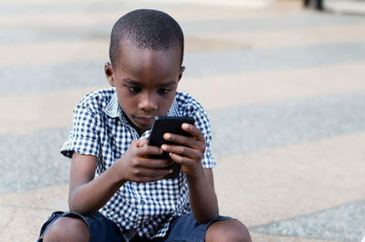 Little boy sitting on the terrace doing games in his mobile phone