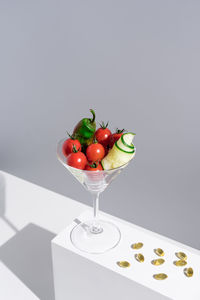 From above of cherry tomatoes with cucumber and green pepper in cocktail glass on stand against white background in studio with sunlight