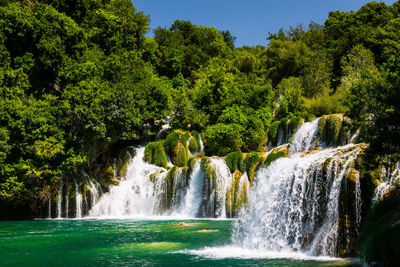 Scenic view of waterfall in forest against clear sky