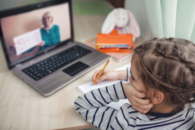 Pretty schoolgirl studying homework math during her online lesson at home, online education concept