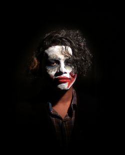 Portrait of young man with face paint standing against black background