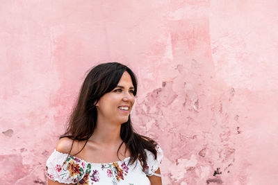 Portrait of smiling young woman against pink wall