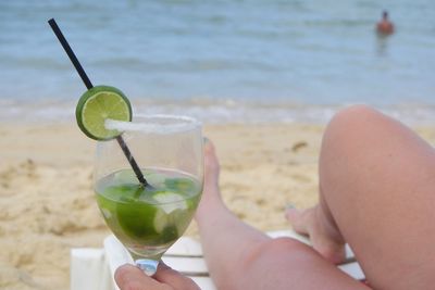 Low section of woman holding lemonade glass while relaxing at beach