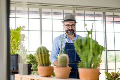 Portrait of senior man holding potted plant in greenhouse