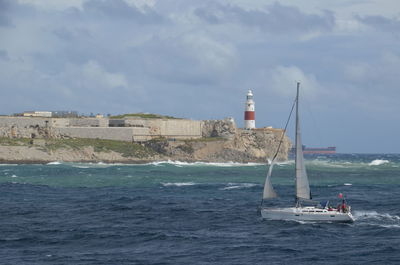 Sailboat sailing on sea by buildings against sky